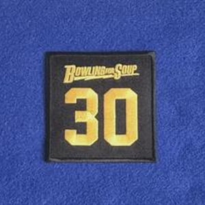 Peut inclure: Un écusson carré en tissu noir arborant le texte doré Bowling For Soup placé au-dessus du grand nombre 30 en lettres dorées. Le motif est brodé avec une bordure nette, offrant un contraste marqué entre le fond sombre et les lettres dorées.