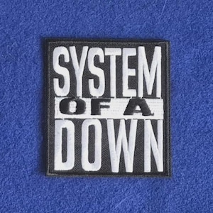 May include: A rectangular black embroidered patch featuring the white text SYSTEM OF A DOWN in a stacked layout. The word SYSTEM is at the top, OF A is centered on a white horizontal bar, and DOWN is at the bottom in bold white lettering.