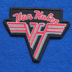 May include: A black embroidered patch featuring the red and grey Van Halen logo with the text Van Halen in a stylised red script font above a large red and grey VH emblem with horizontal wings, all outlined in a thick black border.
