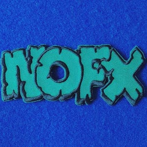 May include: A teal embroidered patch featuring the text NOFX in a jagged, stylised font with a thick black border. The letters have a textured appearance and are outlined in black thread, creating a bold, high-contrast graphic design.