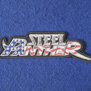 May include: An embroidered fabric patch featuring the text STEEL PANTHER in a stylised font. The letters are filled with a pattern resembling the American flag, with blue and white stars on the left and red and white stripes on the right.