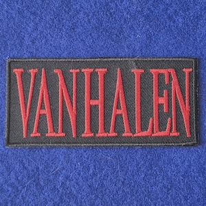 May include: A rectangular embroidered patch featuring a black background with the text VAN HALEN stitched in bold red capital letters. The patch has a black stitched border and is designed for application onto fabric surfaces.