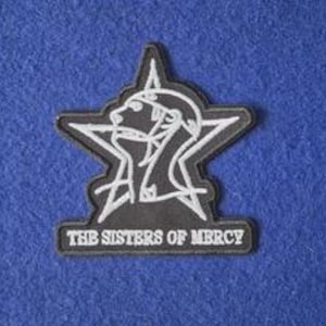 Peut inclure: Un écusson brodé noir présentant le contour d'une étoile blanche et la silhouette stylisée d'un profil de visage. Sous l'étoile, le texte THE SISTERS OF MERCY est brodé en lettres capitales blanches. L'écusson possède une bordure noire.