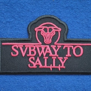 May include: A rectangular black embroidered patch featuring a pink stylised bull head icon above the text SVBWAY TO SALLY in pink capital letters. The patch has a black border and a distinct shape with a rounded top section centred above the text.