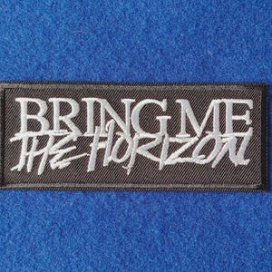 May include: A rectangular black embroidered patch featuring the white text BRING ME THE HORIZON. The top line displays the words BRING ME in a clean serif font, while the bottom line features THE HORIZON in a stylised, handwritten script.