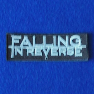 Könnte beinhalten: Ein rechteckiger, schwarz bestickter Aufnäher mit dem Text FALLING IN REVERSE in hellblauem Garn. Die Schrift ist in zwei Zeilen angeordnet, wobei eine horizontale Linie durch die Mitte des Textes über den gesamten Aufnäher verläuft.