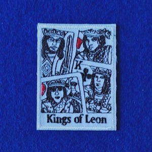May include: A rectangular embroidered patch featuring a white background with black line art depicting four playing card-style portraits of individuals wearing crowns. The text Kings of Leon is printed in black at the bottom of the patch.