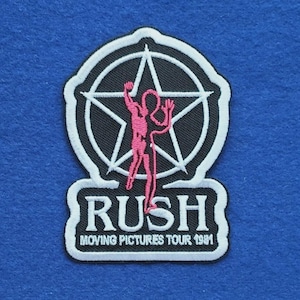 May include: A black and white embroidered patch featuring a star emblem with a pink silhouette of a person inside. Below the emblem, the text reads RUSH MOVING PICTURES TOUR 1981 in white lettering against a black background with a white border.