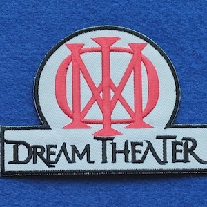 May include: An embroidered patch featuring the red Dream Theater logo symbol centred above the text DREAM THEATER in black lettering on a white background with a black border, designed for application to fabric surfaces.