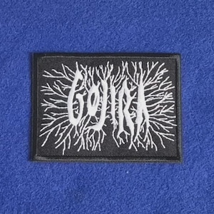 May include: A rectangular black embroidered patch featuring the white text GOJIRA in a stylised, jagged font. The lettering is surrounded by intricate, branching white line patterns that resemble tree roots or nerve endings, all bordered by a black stitched edge.
