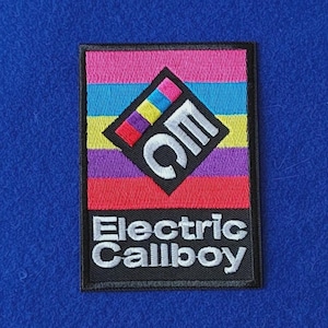 May include: A rectangular embroidered patch featuring horizontal stripes in pink, blue, yellow, purple, and red. A black diamond shape sits in the center with the white letters EC and the text Electric Callboy in white below the stripes.