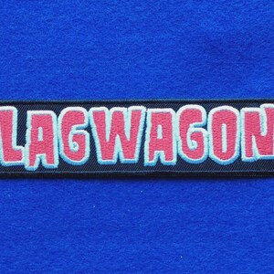 May include: A rectangular embroidered patch with a black background and the word LAGWAGON stitched in pink letters with a light blue outline. The patch features a thick black border and is designed for attachment to fabric items.