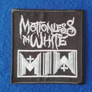 May include: A square black embroidered patch featuring the white text Motionless In White in a stylised font above a rectangular border containing the white letters MIW with small cross symbols integrated into the design.