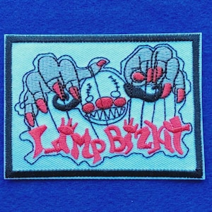 May include: A rectangular embroidered patch with a light blue background and a black border. The design features two hands with red fingernails manipulating a clown face puppet with strings. The text "Limp Bizkit" is embroidered in red below.