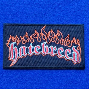 Può includere: Una toppa rettangolare ricamata con sfondo nero che presenta la parola hatebreed in lettere stilizzate rosse e azzurre. Il testo è sormontato da un disegno di fiamme arancioni che copre la larghezza della toppa con un bordo nero.