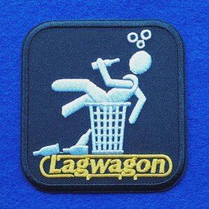 May include: A square embroidered patch with rounded corners featuring a dark blue background. It depicts a white stick figure sitting in a bin, holding a bottle, with two bottles on the ground and the yellow text Lagwagon at the bottom.