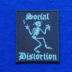 Könnte beinhalten: Ein rechteckiger, schwarzer, bestickter Aufnäher mit einem hellblauen Skelett, das einen Hut trägt, raucht und ein Getränk hält. Der Text Social Distortion ist in hellblauer gotischer Schrift über und unter dem Skelett eingestickt.