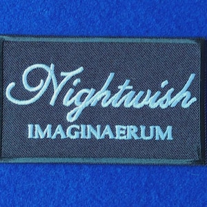 May include: A rectangular black embroidered patch featuring the word Nightwish in a white cursive script font, with the word IMAGINAERUM printed in white capital letters directly underneath. The patch has a black stitched border.