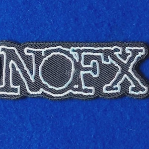 Könnte beinhalten: Ein rechteckiger gestickter Aufnäher mit dem Text NOFX in einer fetten, stilisierten Schriftart. Die Buchstaben sind weiß mit einer dünnen hellblauen Umrandung auf schwarzem Hintergrund mit einem schwarzen Rand.