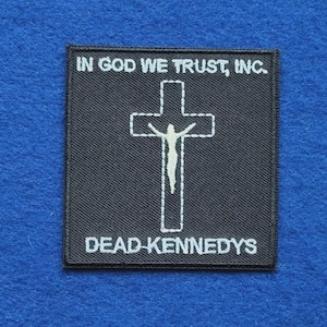 Puede incluir: Un parche cuadrado bordado en negro que presenta una cruz blanca cosida con una figura de Jesús. El texto IN GOD WE TRUST, INC. está bordado en blanco en la parte superior y el texto DEAD KENNEDYS está bordado en blanco en la parte inferior.