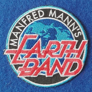 May include: A circular embroidered patch featuring a black background with a light blue globe graphic. The text MANFRED MANN'S is stitched in white along the top border, while the words EARTH BAND are embroidered in bold red across the center.