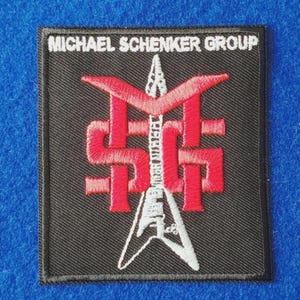 Peut inclure: Un écusson brodé carré sur fond noir avec le texte blanc MICHAEL SCHENKER GROUP en haut. Le centre présente un logo MSG rouge entrelacé avec un motif blanc représentant une guitare électrique en forme de V pointée vers le haut.