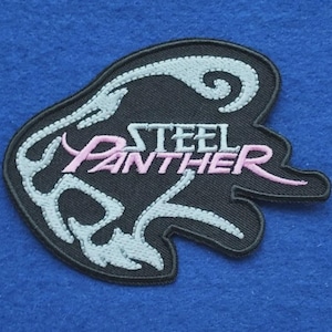 以下が含まれることがあります： ピンクと白の文字で「Steel Panther」と書かれた黒い刺繍ワッペン。デザインには、テキストを囲むパンサーの頭の形をした白いスタイリッシュな輪郭が含まれており、黒い縁取りと黒い布地の背景が特徴です。