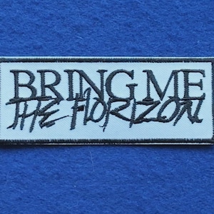 Puede incluir: Un parche rectangular bordado con fondo blanco y borde negro. El texto BRING ME está bordado en una fuente negra sans-serif en negrita, con la palabra THE HORIZON bordada debajo en una escritura negra estilizada y hecha a mano.