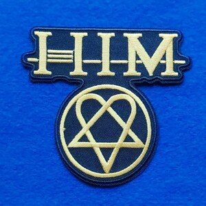 Op de afbeelding: Een donkerblauwe geborduurde patch met de tekst HIM in gouddraad boven een cirkelvormig embleem. Het embleem bevat een gouden heartagram-symbool, een combinatie van een hartvorm en een vijfpuntige ster, op een donkerblauwe achtergrond.