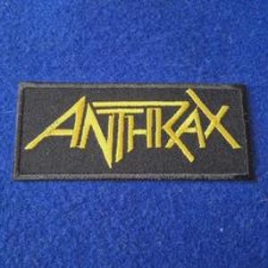 Könnte beinhalten: Ein rechteckiger bestickter Aufnäher mit dem Wort ANTHRAX in fetter, gelber, stilisierter Schrift. Der Text ist auf einem einfarbigen schwarzen Hintergrund zentriert, mit einem dünnen schwarzen Rand um die rechteckige Form des Aufnähers.