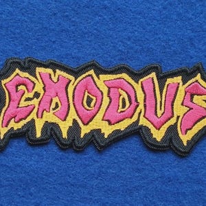 May include: A rectangular embroidered patch featuring the word EXODUS in stylised pink lettering with a yellow outline and a thick black border. The design has a jagged, irregular shape with drip-like details along the bottom edge of the text.