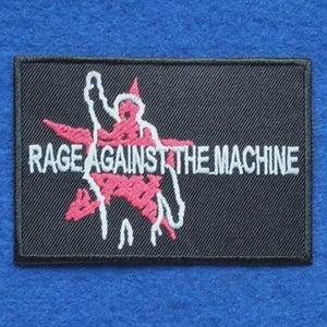 May include: A rectangular black embroidered patch featuring a pink star graphic with a white outline of a person raising one arm. The text RAGE AGAINST THE MACHINE is embroidered in white capital letters across the centre of the design.