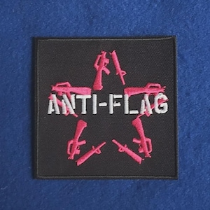 May include: A square black embroidered patch featuring a pink star shape formed by rifle silhouettes. The text ANTI-FLAG is stitched in white across the centre of the star. The patch has a black border and is designed for application to fabric.
