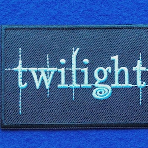 May include: A rectangular embroidered patch featuring a dark navy blue background with the word twilight stitched in light blue thread. The lettering includes vertical lines extending through the letters and a spiral detail on the letter g.