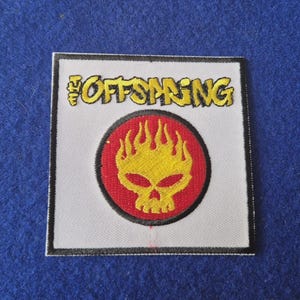 Puede incluir: Un parche bordado cuadrado con fondo blanco y borde negro. El texto THE OFFSPRING está bordado en amarillo sobre un emblema circular que contiene un gráfico de calavera llameante amarilla centrado en un fondo rojo con borde negro.
