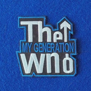 May include: A rectangular embroidered patch with a black background and a blue border. The text reads "The" in light blue, "MY GENERATION" in blue, and "WHO" in light blue, with an upward-pointing arrow integrated into the letter "h" and a circle.