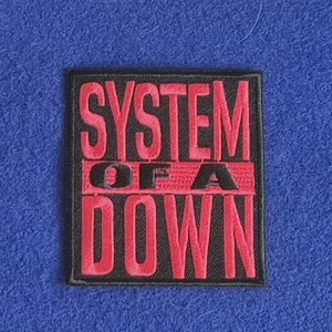 Op de afbeelding: Een rechthoekige geborduurde patch met de tekst SYSTEM OF A DOWN in vetgedrukte rode letters. Het woord SYSTEM staat op de bovenste regel, OF A is gecentreerd op een rode horizontale balk en DOWN staat op de onderste regel, alles op een zwarte achtergrond.