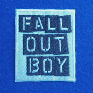 May include: A rectangular embroidered patch featuring the text FALL OUT BOY in white block letters. The letters are arranged in three rows on a dark background, enclosed within a light-coloured border, creating a clear and bold graphic design.