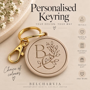 May include: A round beige keyring with a gold-tone metal lobster clasp and ring. The keyring features an embossed letter B and a floral branch design. Text on the image includes Personalised Keyring, Your design, your way, Choice of colours, Belcharvia, Contemporary objects, digitally crafted, and icons for initials, names, titles, business logos, and gifts.