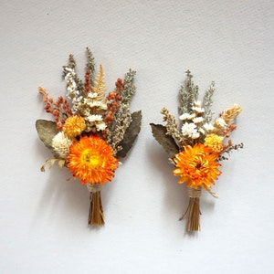 May include: Two small bouquets of dried flowers with orange and white blooms. The bouquets are tied with twine and have a rustic, natural look.