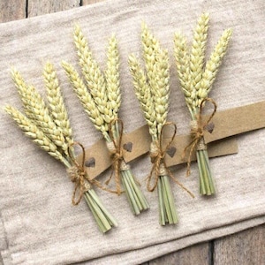 May include: Four small bundles of dried golden wheat stalks, each tied with thin brown twine. Attached to each bundle is a rectangular brown kraft paper tag featuring a small, dark brown heart icon printed near the center of the paper strip.