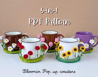 Puede incluir: Un patrón PDF 5 en 1 para posavasos Bloomin Pop up con diseños de flores de ganchillo. La imagen muestra cuatro tazas sobre bases de ganchillo verde decoradas con margaritas blancas, rosas rojas, tulipanes rosas y girasoles tridimensionales.