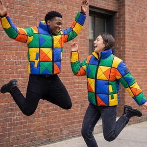 Puede incluir: Una chaqueta acolchada con un vibrante patrón geométrico de bloques multicolor en colores primarios rojo, amarillo, verde y azul. La chaqueta tiene cuello alto, cremallera frontal completa, mangas largas y bolsillos laterales con ribete negro.