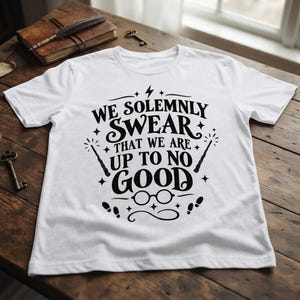 May include: A white short-sleeved t-shirt featuring black graphic text that reads WE SOLEMNLY SWEAR THAT WE ARE UP TO NO GOOD. The design includes illustrations of a lightning bolt, two wands, round glasses, and small footprints surrounding the text.