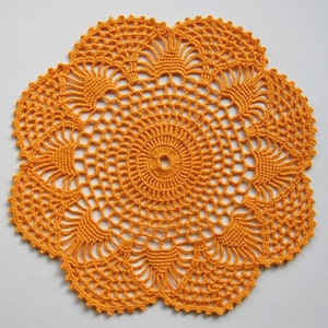 May include: A crocheted doily in a bright orange colour with a circular design. The doily has a delicate, intricate pattern with a central circle and radiating spokes.