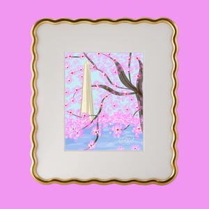 May include: A framed illustration of a white obelisk with a pink cherry blossom tree in the foreground. The background is a light blue sky with white clouds. The frame is gold with a scalloped edge.