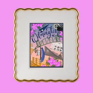 May include: Framed art print featuring a colorful illustration of Wilmington, NC. The artwork includes a bridge, a ship, and the text "Wilmington NC". Pink flowers and a film reel are also depicted in the artwork. The frame has a gold edge and a white interior.