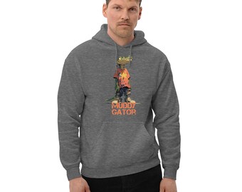 May include: A dark heather gray hooded sweatshirt featuring a graphic of a green alligator wearing a red t-shirt with a yellow star, blue shorts, and sneakers. Below the alligator, the text MUDDY GATOR is printed in a distressed orange font.
