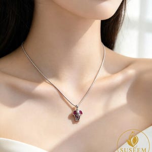May include: A silver-toned necklace featuring a small elephant-shaped pendant. The elephant pendant is accented with bright pink stones on its ears and has a polished metallic finish. The pendant hangs from a thin, delicate silver-toned chain.