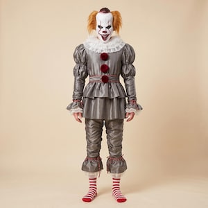 May include: A clown costume featuring a grey satin-like tunic with puffed sleeves, a white ruffled collar, and three dark red pom-poms. The outfit includes matching grey trousers with ruffled cuffs, red and white striped socks, and a clown mask.